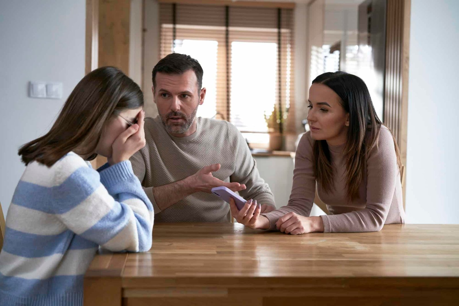 Caucasian parents arguing with teenager girl and holding mobile phone in hands Caucasian parents arguing with teenager girl and holding mobile phone in hands