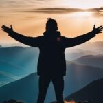 Person with arms spread on mountain at sunset.