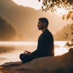 Man meditating by lake at sunset.