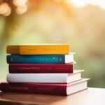 Stack of colorful books on wooden table at sunset.