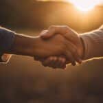 Two people handshake in sunset light.