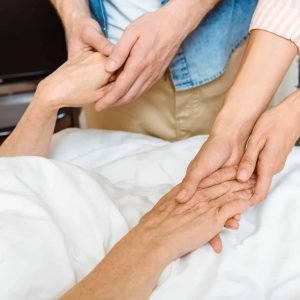 partial view of young people hands holding hands of elderly woman lying on hospital bed
